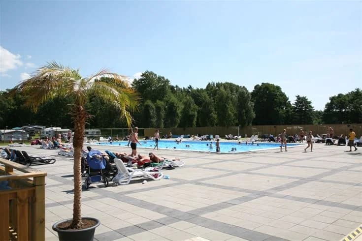 En solig dag vid en uppvärmd utomhuspool på Saxnäs camping. Flera glada besökare njuter av bad och avkoppling i en naturskön miljö. Perfekt för familjesemestern med rekreation och fritidsaktiviteter.