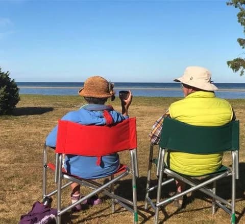 En person sitter avslappnat i en hopfällbar stol på en grön gräsmatta vid Wikegårds Semesterby & Ställplatscamping, omgiven av somrig utomhusmiljö och fritidsmöbler.