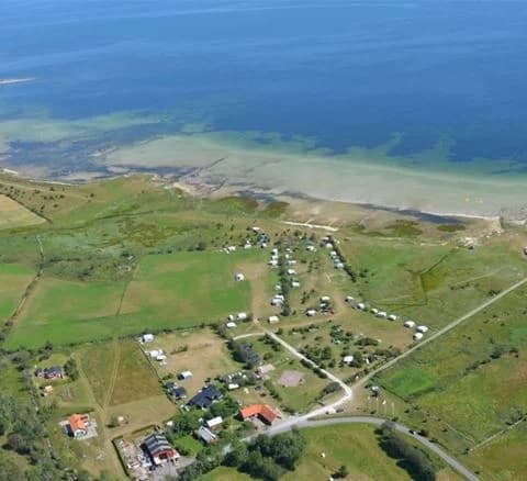 Luftvy över Wikegårds Semesterby & Ställplatscamping, som visar en kustnära by med bostadsområden och landtomter, belägen vid havskusten.