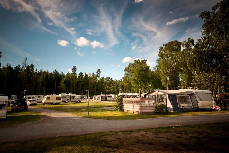 En campingplats vid Bredsands bad & camping, omgiven av grönskande träd, med flera husvagnar parkerade på området i närheten av en rekreationsyta.