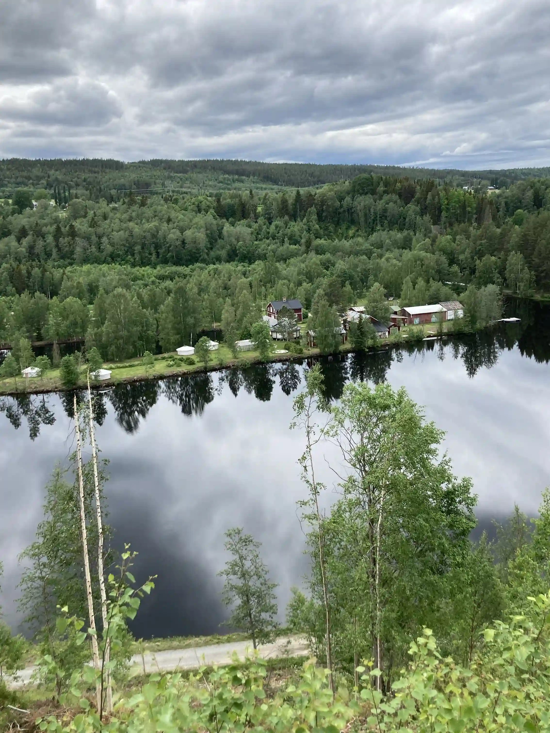 En naturskön vy över Näsåkers camping & stugby, omgiven av en grönskande skog och en stilla sjö.