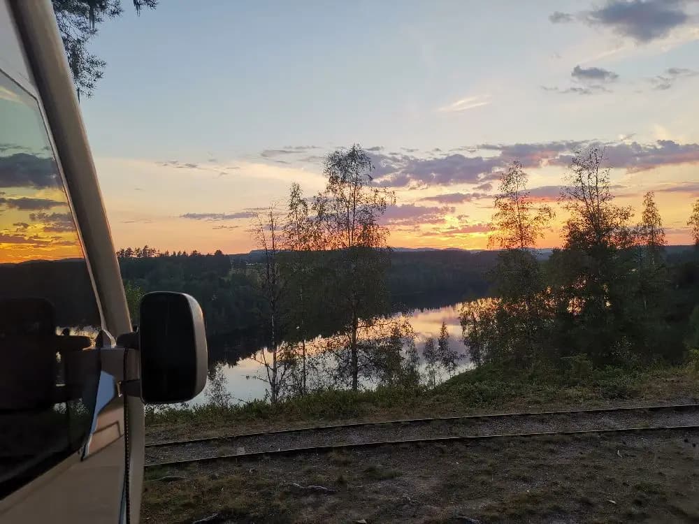 En bild av Näsåkers camping & stugby i skymningen, där en vacker solnedgång färgar himlen i varma toner. Atmosfären är lugn och fridfull, med speglingar av det gyllene ljuset synliga.