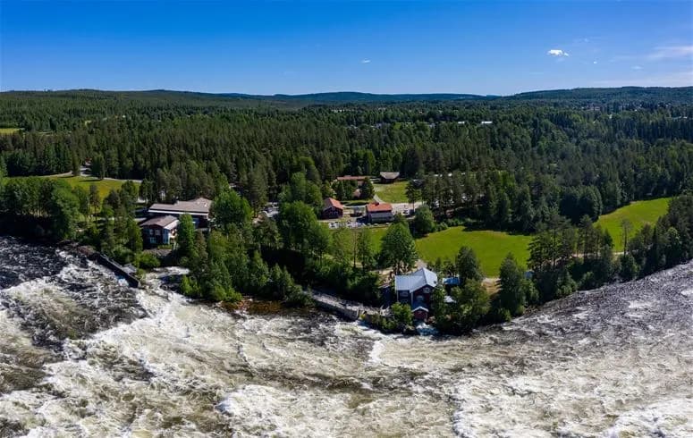 En forsande älv omgiven av tät barrskog vid Vindelforsarnas camping, med virvlande strömmar och små vattenfall i det varierande landskapet.