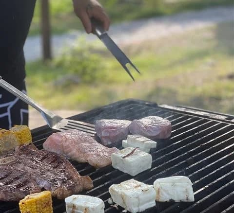 En närbild av en grill utomhus på Waxholms camping, där kött steks över öppen låga.