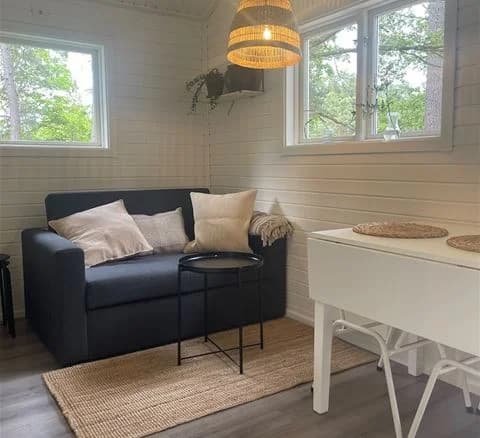 Bild av en modern och inbjudande interiör på Waxholms camping. Trägolv pryder rummet och en bekväm soffa står placerad i hörnet. Ljusa träelement kompletterar den stilrena designen av vardagsrummet.