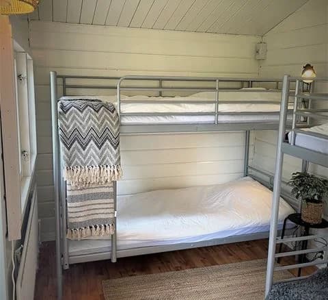 En enkel och rustik sovsal med våningssängar i trä, trägolv och enkel inredning på Waxholms camping.