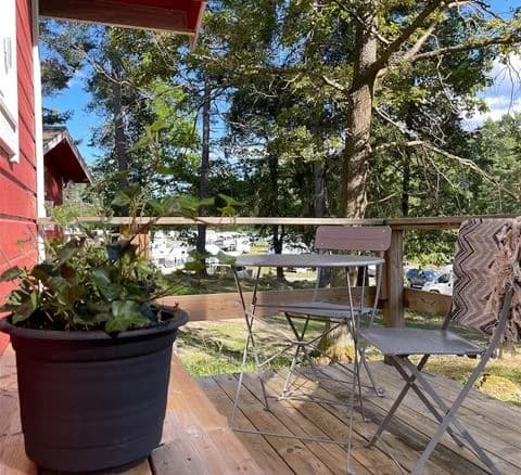 Bild av en träaltan på Waxholms camping med utemöbler: ett bord med stolar i trä. Några blomkrukor dekorerar området, och i bakgrunden syns en lantlig bakgårdsmiljö.