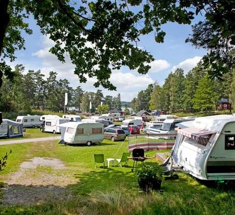 En grön campingplats med välklippt gräsmatta där flera husvagnar och husbilar står parkerade i naturskön miljö.