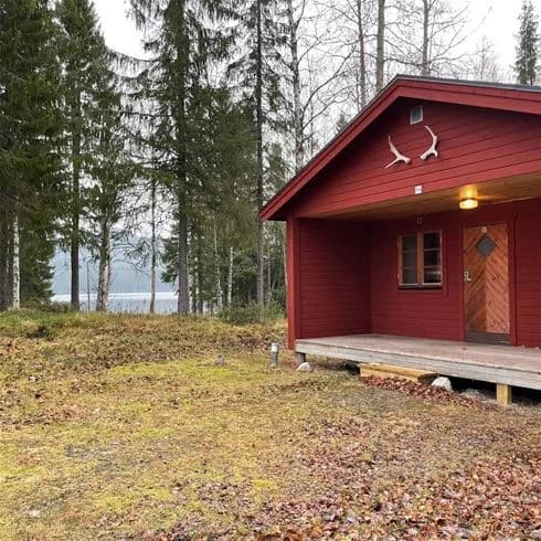 En pittoresk stuga av trä i ett naturskönt, landsbygdsområde vid Valsjöbyns Camping, omgiven av grönska och mindre byggnader.