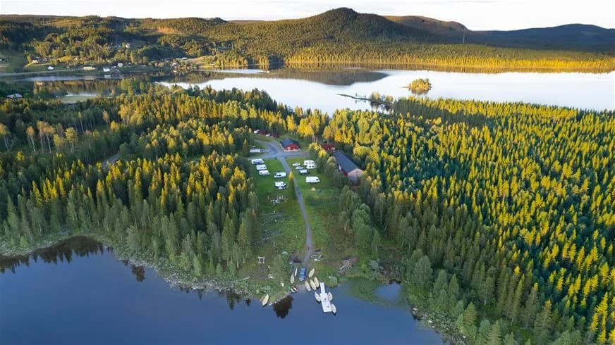 Alt-text: En naturskön vy vid Valsjöbyns camping med en sjö omgiven av frodig grönska och träd.