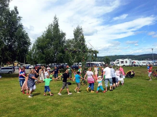 En grupp människor njuter av fritiden på Lövekulle camping, omgivna av grönt gräs och husbilar i bakgrunden. Stämningen är avslappnad och inbjudande.