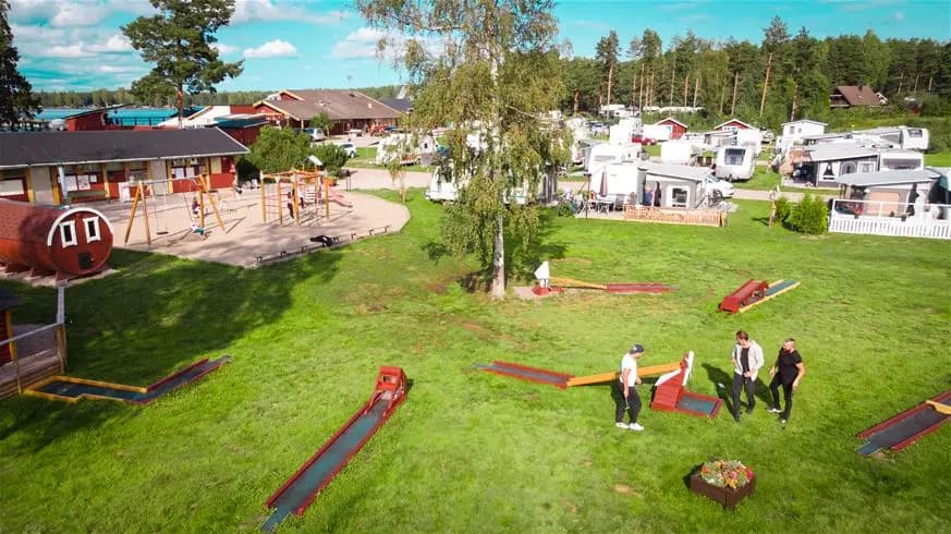 En grön park med lekplatsutrustning vid Årsunda Strandbad, omgiven av en öppen gräsmatta och fridfull rekreationsmiljö.