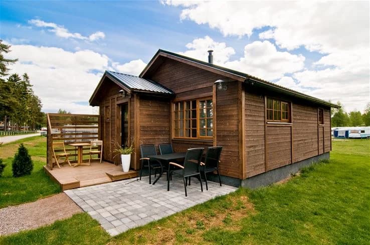 En trästuga vid Årsunda strandbad, omgiven av frodig grönska och med en träddörr.