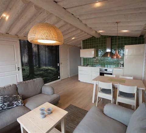 Ett interiört rum på Torsby Camping med träinredning. Trätak och träväggar kompletterar det ljusa trägolvet. Rummet har flera ljuskällor, inklusive en central ljuskrona som hänger från taket.