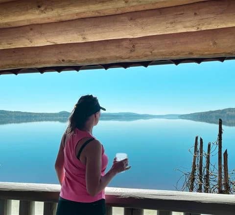 En fridfull sjö med klarblått vatten omgiven av grönskande strandlinje vid Torsby Camping, perfekt för avkoppling och semester.