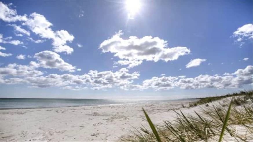 En solig dag vid Bingsmarkens camping med klarblå himmel, moln och havet i bakgrunden.