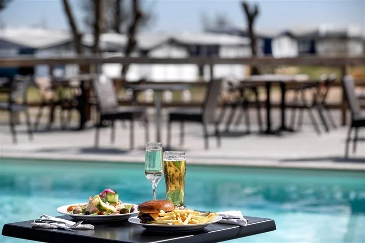 Campingplats med poolområde, solstolar och parasoller, utemöbler vid poolen.