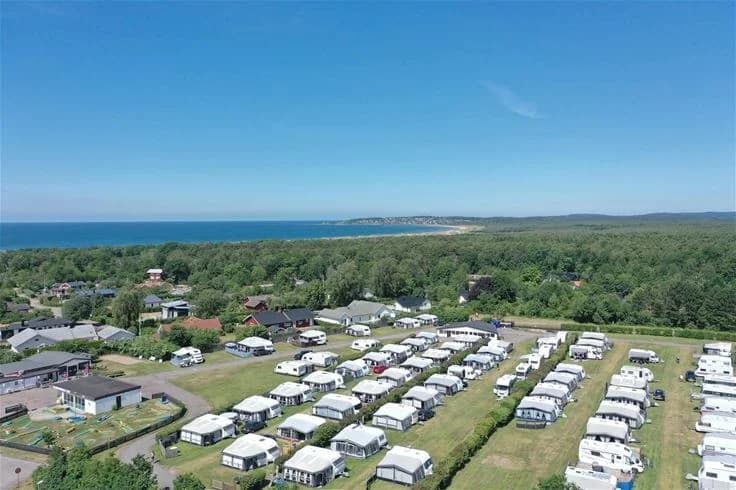 Flygbild över Vilshärads camping som visar ett naturskönt kustlandskap med hav, bukt och kustlinje. Sandstränder och grönskande områden omger campingen i ett inbjudande semestermål.