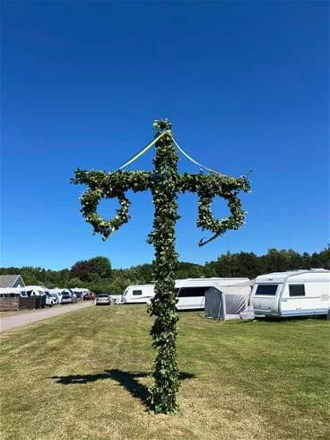 En träpol med ett enkelt kors står i ett naturligt skogslandskap, symboliserande en lantlig och fridfull atmosfär vid Vilshärads camping.