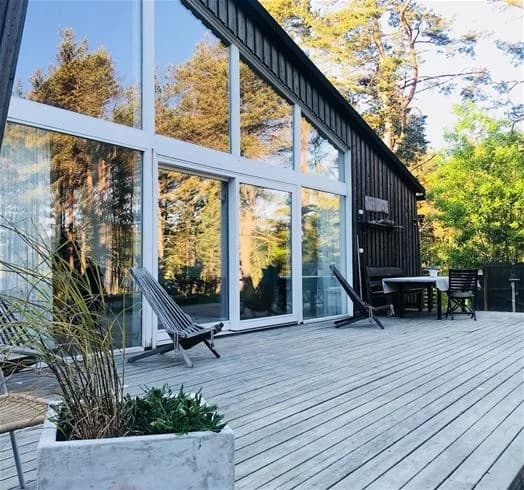 Alt-text: En stuga byggd av trä med breda plankor och sidoklädnad vid Hölick Havsresort. Framsidan har en träveranda och en ytterdörr, vilket bidrar till stugans inbjudande atmosfär.