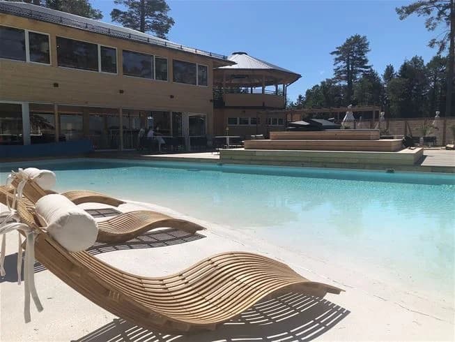 En solig dag vid en stor utomhuspool på Hölick Havsresort, omgiven av bekväma solstolar och skuggande parasoller. Poolområdet ligger vid resortens moderna villor, med fokus på avkoppling och naturnära upplevelser.