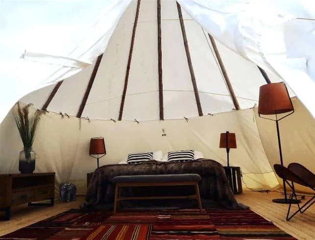 En mysig glampingmiljö på Hölick Havsresort med en välbäddad säng utrustad med kuddar och sänglinne inuti ett tält, omgiven av mjuk belysning och campingmöbler.