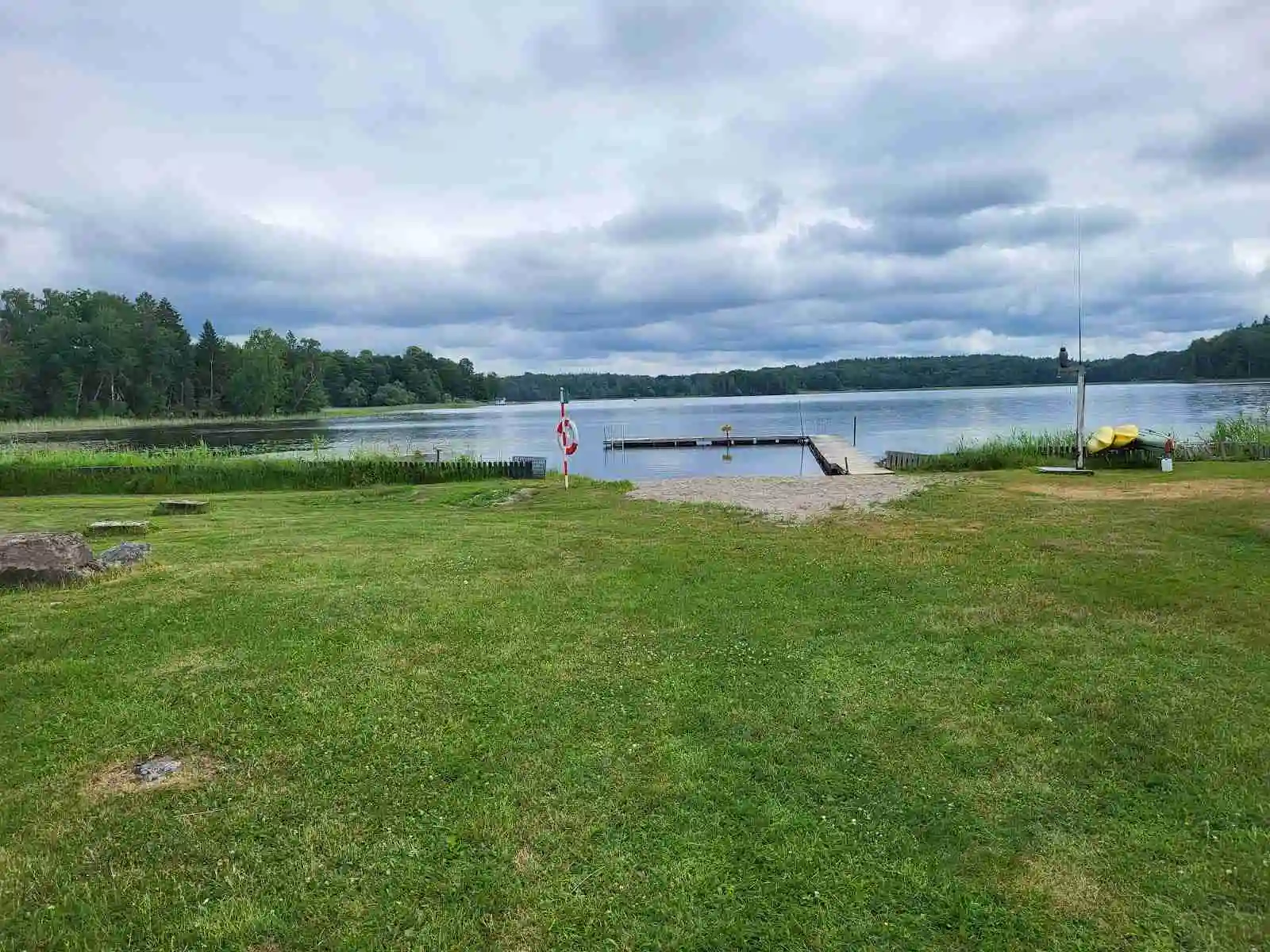 En grön gräsmatta sträcker sig mot en stilla sjö under en himmel med lätta moln vid Österby Camping.