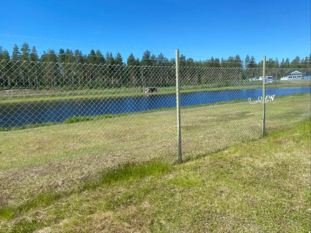 En vidsträckt åker med ett stängsel av kedjelänk och nätverk, omgiven av ängar och gräsmarker på Fromhedens camping.