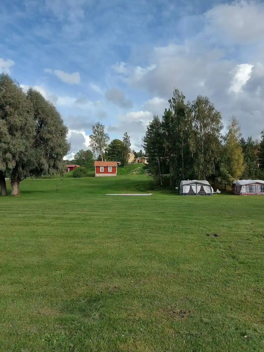 Bild av Uskavigårdens camping med en vidsträckt, grön äng omgiven av träd. Ljusa gräsmattor och öppna fält skapar en inbjudande atmosfär, perfekt för rekreation och friluftsliv.