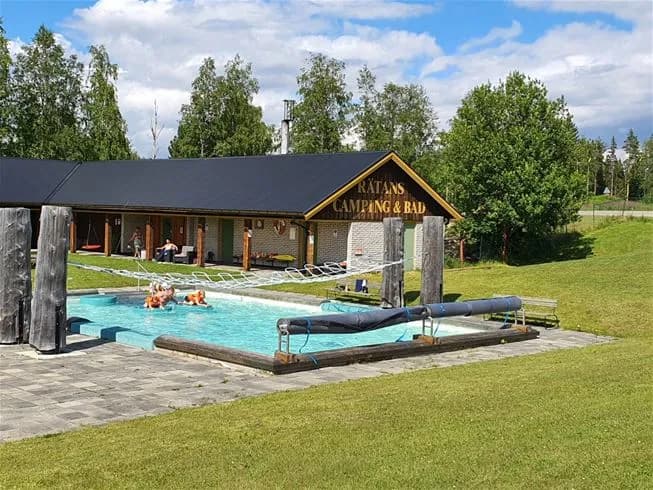 En utomhuspool omgiven av gröna områden och skuggiga platser på Rätans camping, en avkopplande miljö i en ekoinriktad semesterort.