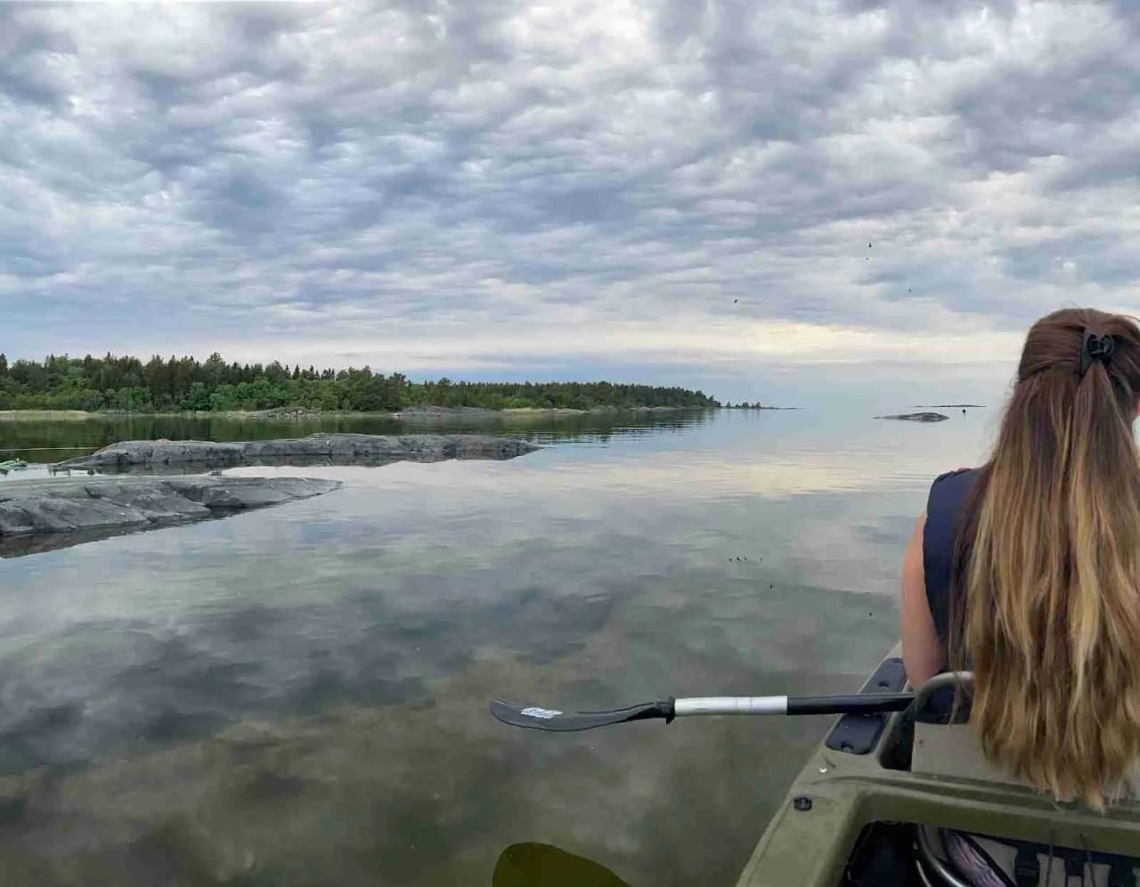 En kustvy med en klar blå himmel och några moln. I förgrunden syns flera färgglada kajaker och båtar vid en campingplats nära stranden. Det är en vacker och avkopplande scen vid havet, perfekt för utomhusaktiviteter som paddling och kanotturer.