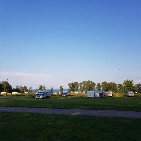En grön campingplats med husvagnar, omgiven av stora gräsytor och en parkmiljö.