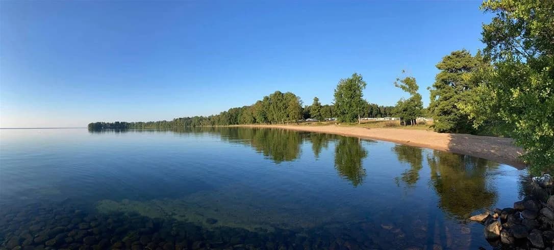 En strandnära campingplats vid vattnet med blå himmel i bakgrunden.