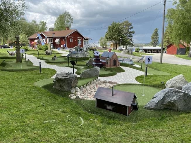 En grönskande campingplats med lekutrustning och välskötta gräsmattor, omgiven av träd och buskar. Perfekt för avkoppling och utomhusaktiviteter.