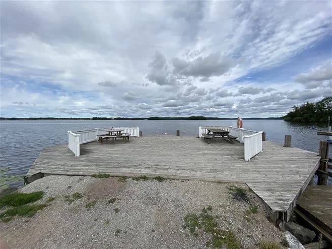 En träbrygga vid Skokloster camping sträcker sig ut över en sjö under en blå himmel med cumulusmoln.