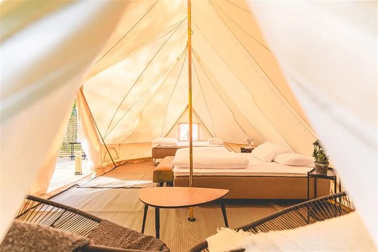 En tältplats med ett stort tält och baldakin på träunderlag vid Vimmerby Camping - Nossenbaden, omgiven av utomhusmöbler för avkoppling i naturen.