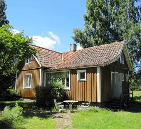 Bild av Bödagårdens camping som visar en grön gräsmatta framför en vit stuga med rött tak. Stugan omges av fler byggnader och en trädkantad tomt som bidrar till en lantlig och hemtrevlig atmosfär.