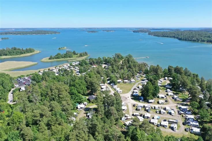 Fågelperspektiv över Trosa havsbad & camping med betoning på vattendraget och kustlinjen, visar en blandning av kustlandskap och campingområden vid sjön.