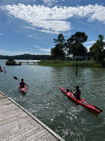 En kajakpaddlare navigerar genom det lugna vattnet vid Trosa havsbad & camping, omgiven av naturskön miljö.
