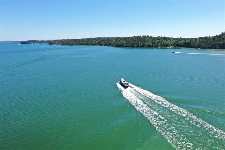 En campingplats vid en kustlinje med flera båtar på vattnet. Havet sträcker sig mot horisonten, och området omges av naturliga vattenresurser.