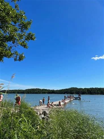 En solig dag vid Trosa havsbad & camping med människor som njuter av utomhusaktiviteter vid sjön.