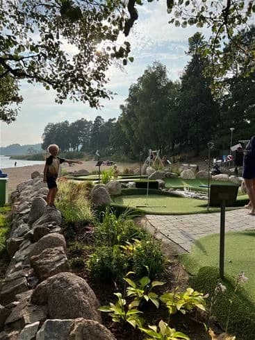 Bild av Trosa Havsbad & Camping som visar en rekreationsområde med en välskött trädgård och parkmiljö. Ett litet dammområde syns, omgivet av grönskande landskapsarkitektur som inbjuder till avkoppling och semesteraktiviteter.