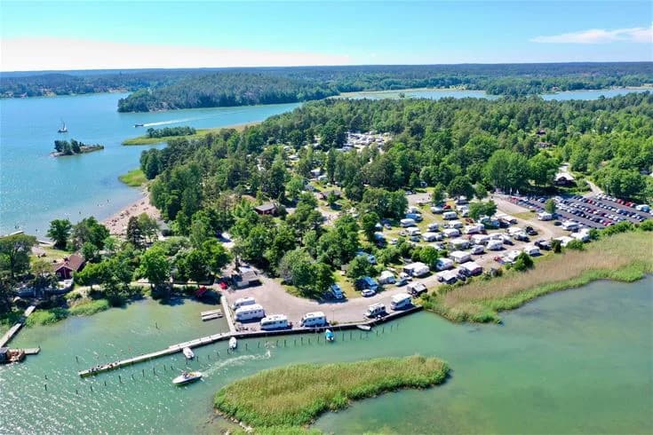 Flygfoto över Trosa Havsbad & Camping som visar en vidsträckt kustlinje med vattendrag och småbåtshamn, omgivet av grönskande natur.