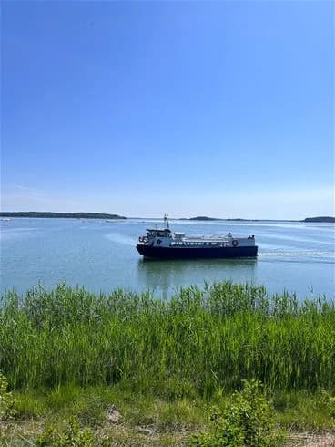 En båt på vattnet nära kusten vid Trosa havsbad & camping, med en molnig himmel i bakgrunden.