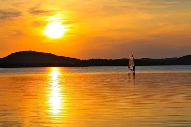 En rofylld sjö vid solnedgången med en glödande orange horisont, belägen vid Camp Viking, ett populärt resmål för naturälskare.