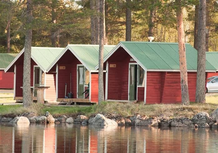 En mysig timmerstuga omgiven av grönska, typisk för Camp Viking, med träfasad och en rustik charm som inbjuder till avkopplande vistelser i naturen.