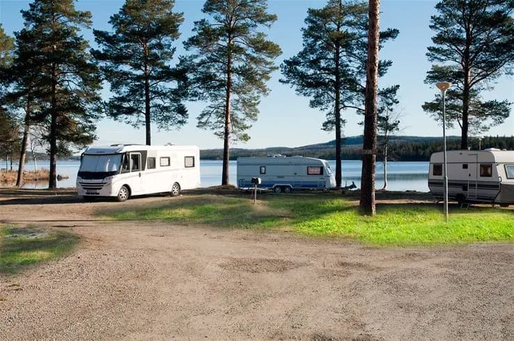 En husbil står parkerad vid en sjöstrand nära Camp Viking, omgiven av naturskön kust med lugnt vatten.