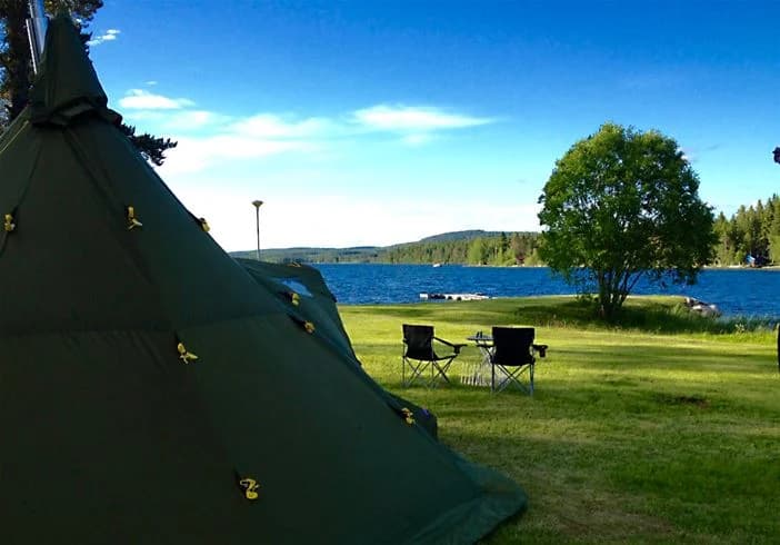 En campingplats vid en sjö med tält och presenning, omgiven av frodig natur.