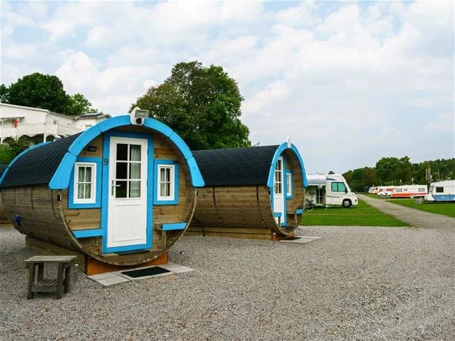 En liten stuga omgiven av frodig grönska på Skotteksgården Camping & Stugby, med en välskött trädgård och parkmiljö som ger en lugn och avkopplande atmosfär.
