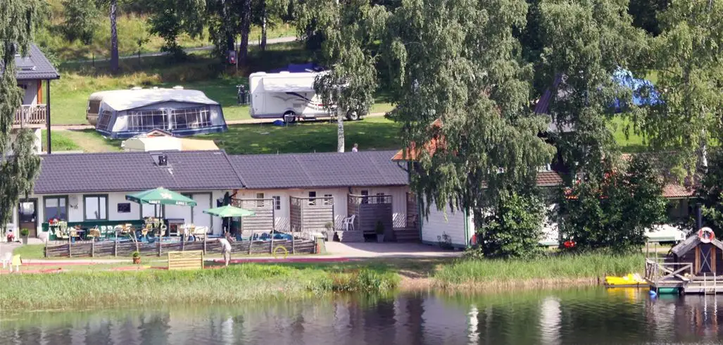 En pittoresk camping med stugor vid en sjö omgiven av frodig vegetation, perfekt för rekreation och avkoppling i naturen.